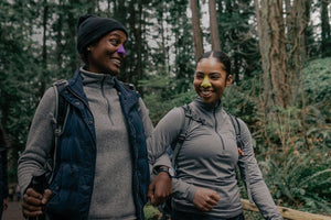 Two smiling women with dark skin wearing best reef safe zinc oxide mineral sunscreen for face while hiking on a trail in the woods